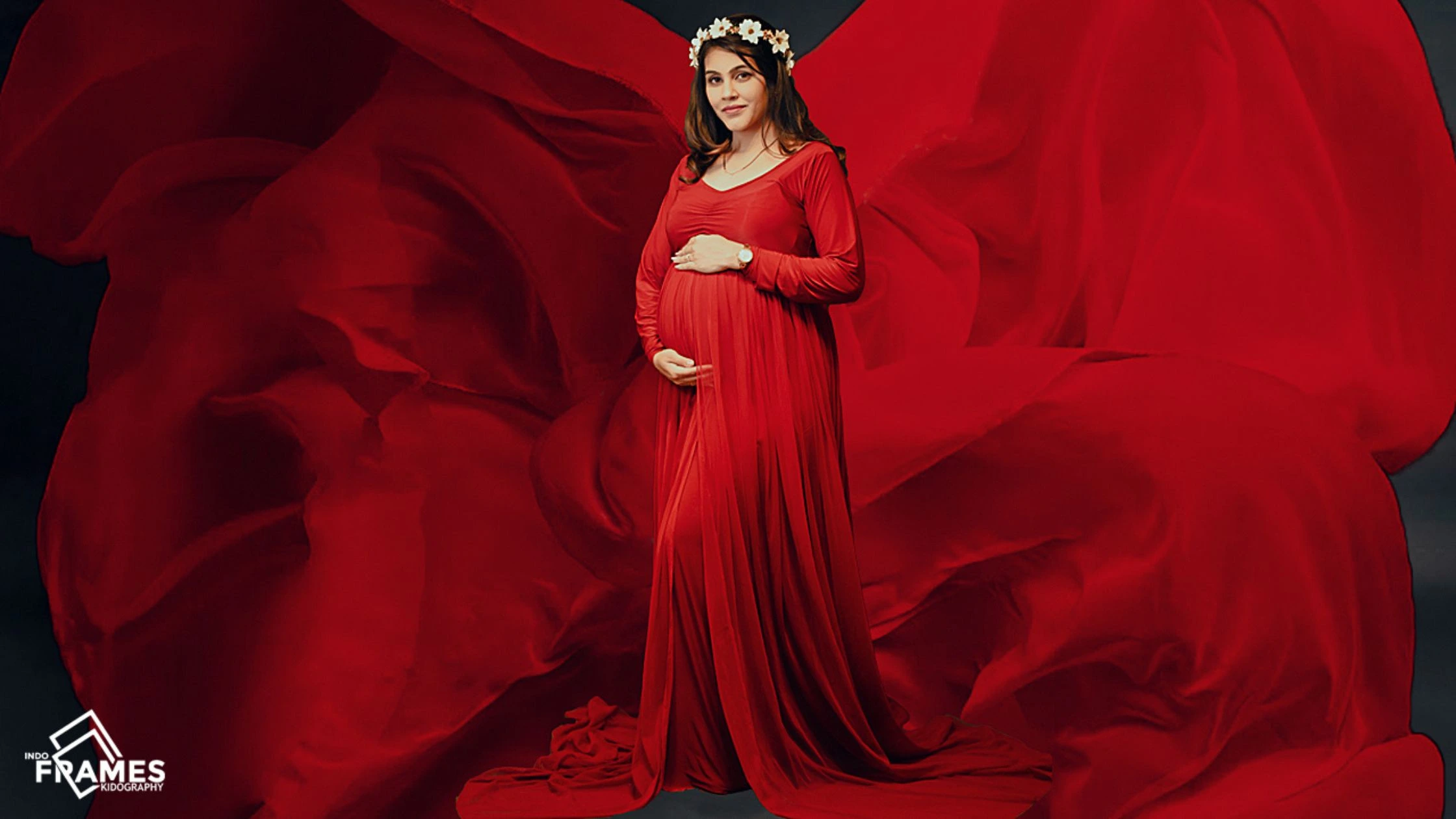 Pregnant woman in elegant red winter maternity gown during studio photoshoot by Indo Frames